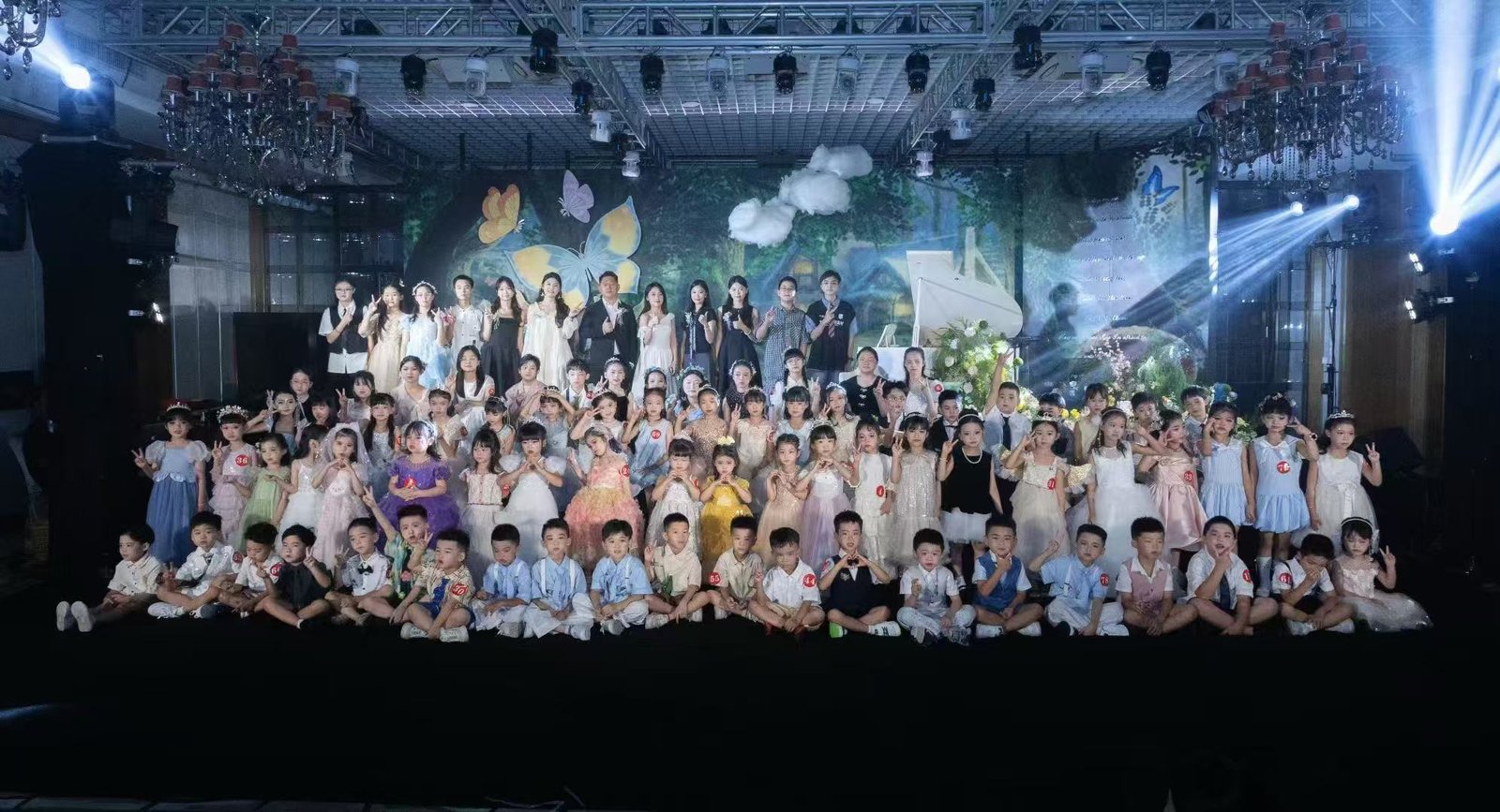 一群穿着演出服的儿童和老师在带有蝴蝶装饰的舞台前合影